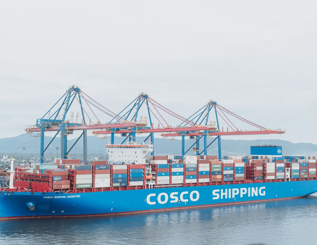 Illustrative stock photo: A cargo ship beside port cranes.